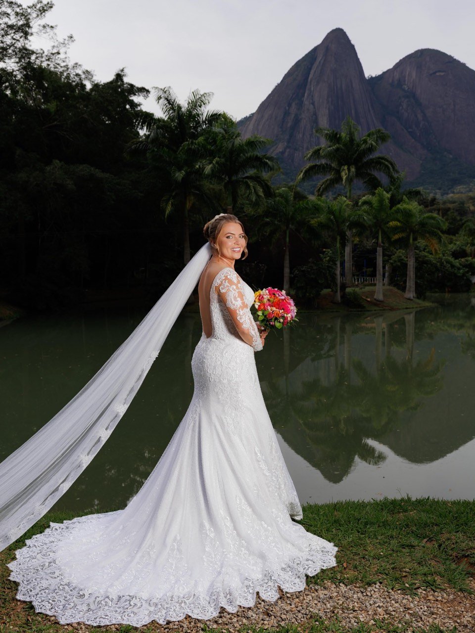 Noiva com vestido sereia de renda e véu longo diante de lago e montanhas